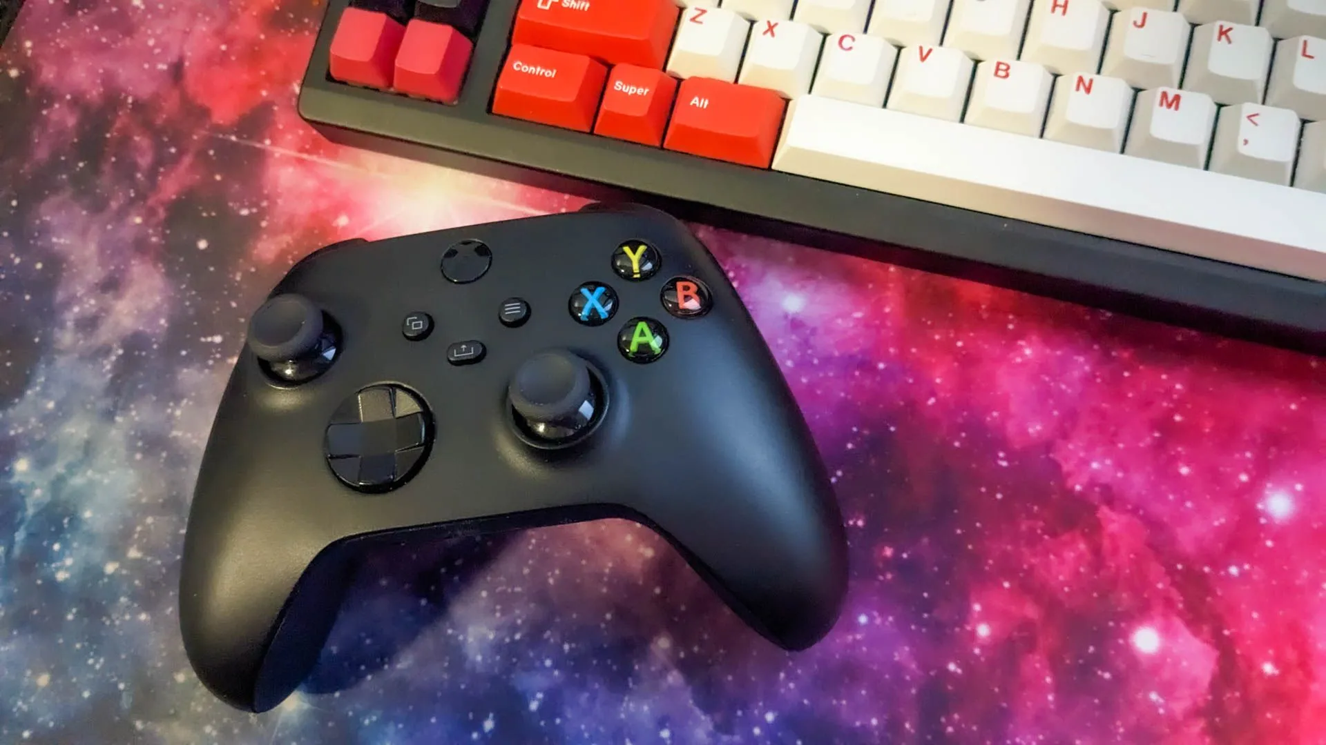 Bộ điều khiển Xbox và bàn phím cơ trên tấm lót chuột lớn, minh họa góc gaming setup.