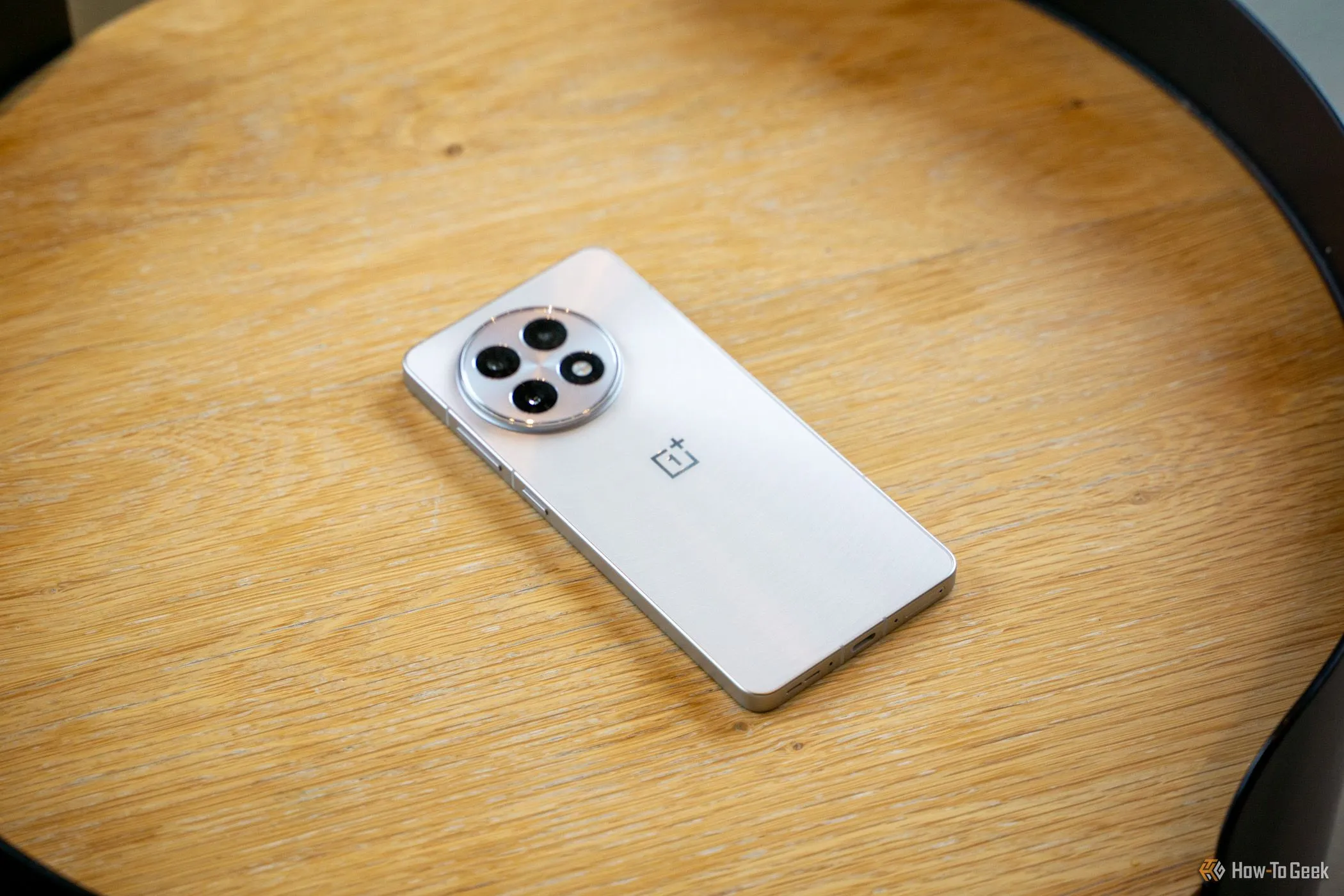 Điện thoại OnePlus 13R màu xanh đen đặt úp trên bàn gỗ, nổi bật cụm camera sau hình tròn với ba ống kính