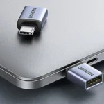 Hai adapter UGREEN USB-C sang USB-A 10Gbps màu xám đang kết nối và nằm trên một chiếc laptop, minh họa khả năng mở rộng cổng kết nối cho Mac Mini.
