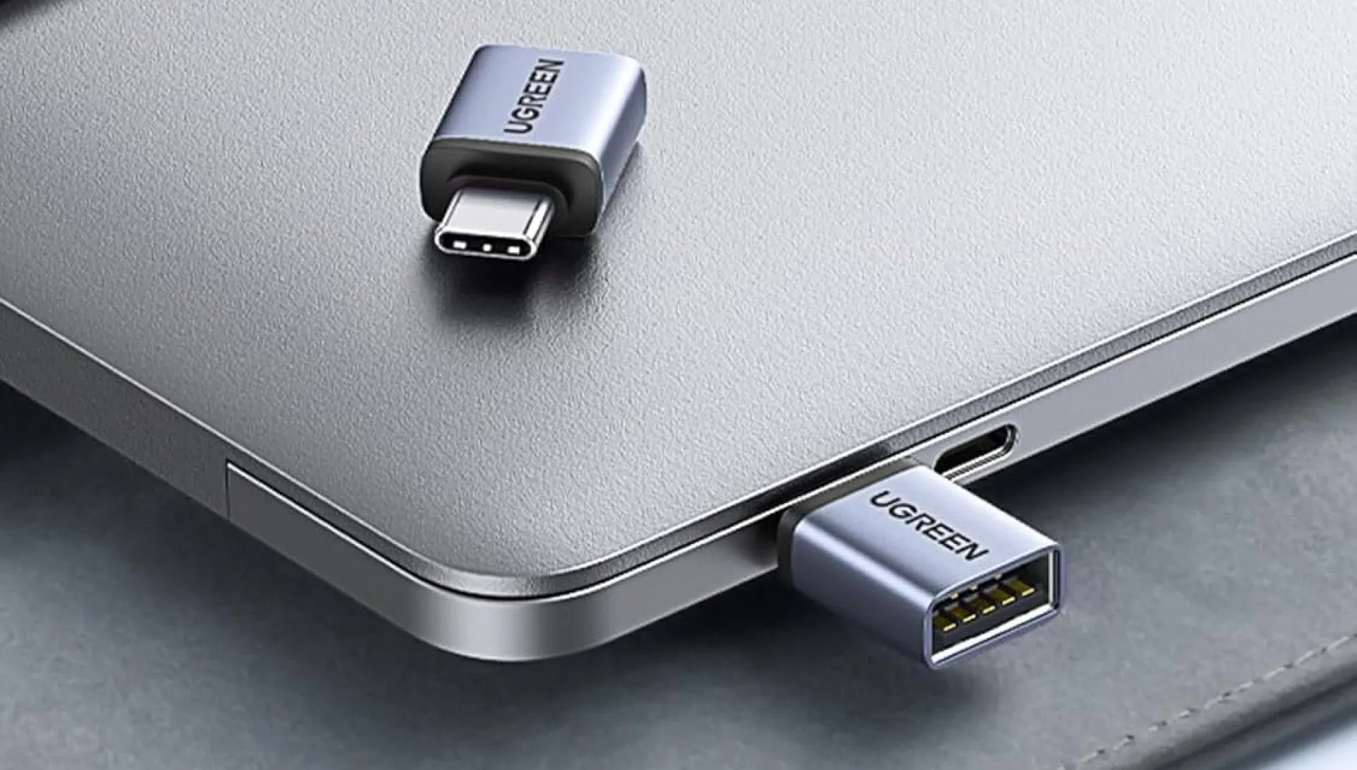 Hai adapter UGREEN USB-C sang USB-A 10Gbps màu xám đang kết nối và nằm trên một chiếc laptop, minh họa khả năng mở rộng cổng kết nối cho Mac Mini.