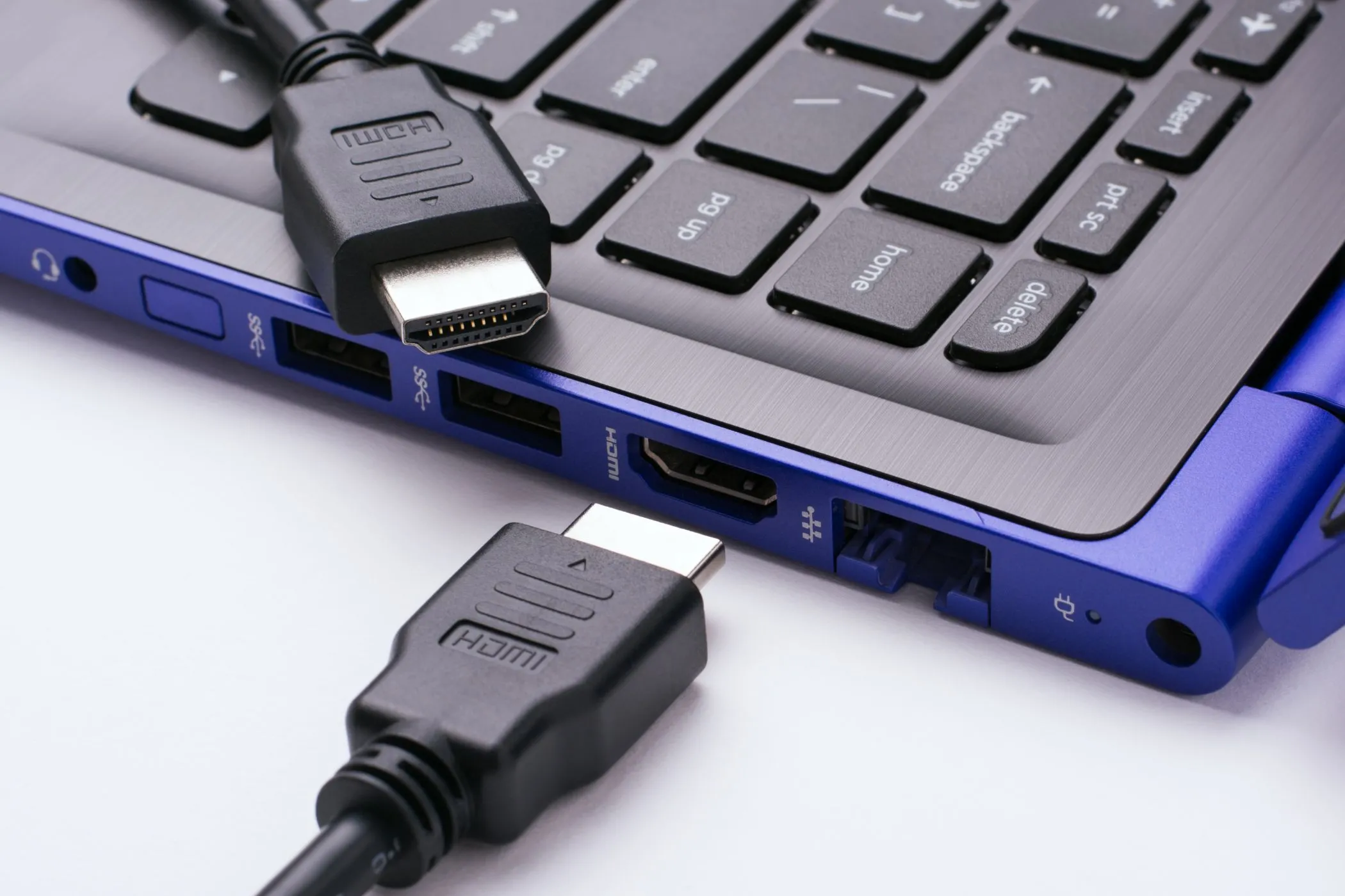 Hai đầu cáp HDMI gần cổng HDMI của laptop hiện đại trên nền trắng