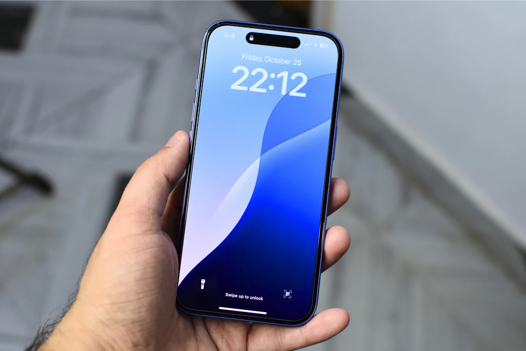 iPhone 16 được cầm trên tay, màn hình hiển thị hình nền màn hình khóa màu xanh lam.