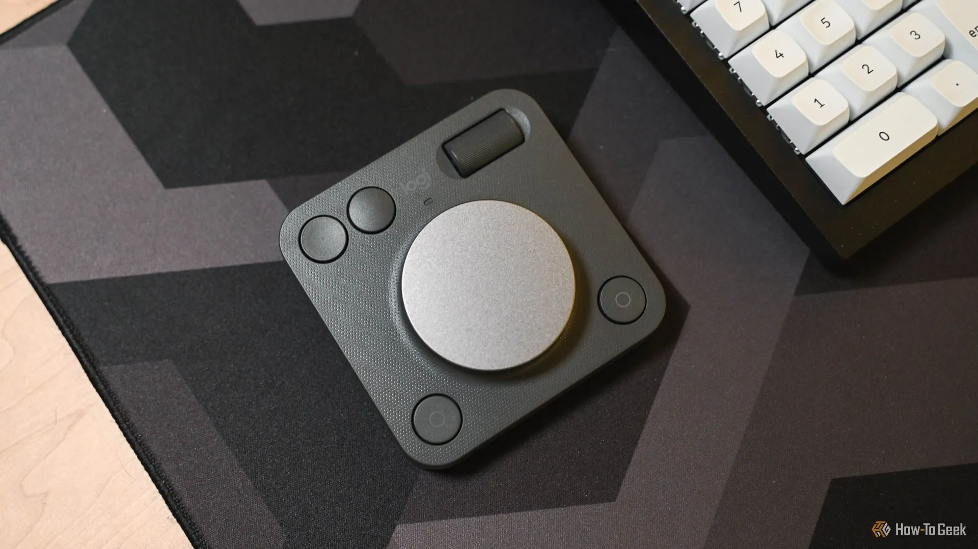 Logitech MX Creative Dialpad được đặt ngay cạnh một bàn phím máy tính thông thường, làm nổi bật kích thước nhỏ gọn và vị trí tiềm năng trên bàn làm việc.