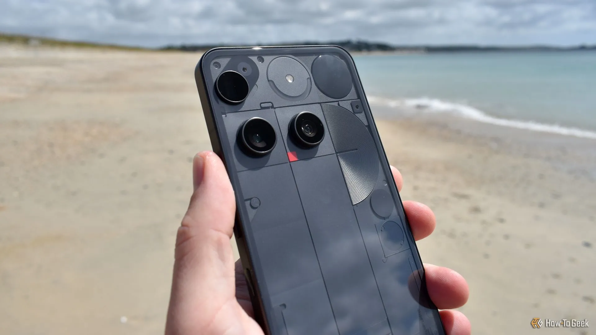 Mặt lưng Nothing Phone (3) và cụm camera ba ống kính trên bãi biển, thể hiện thiết kế độc đáo