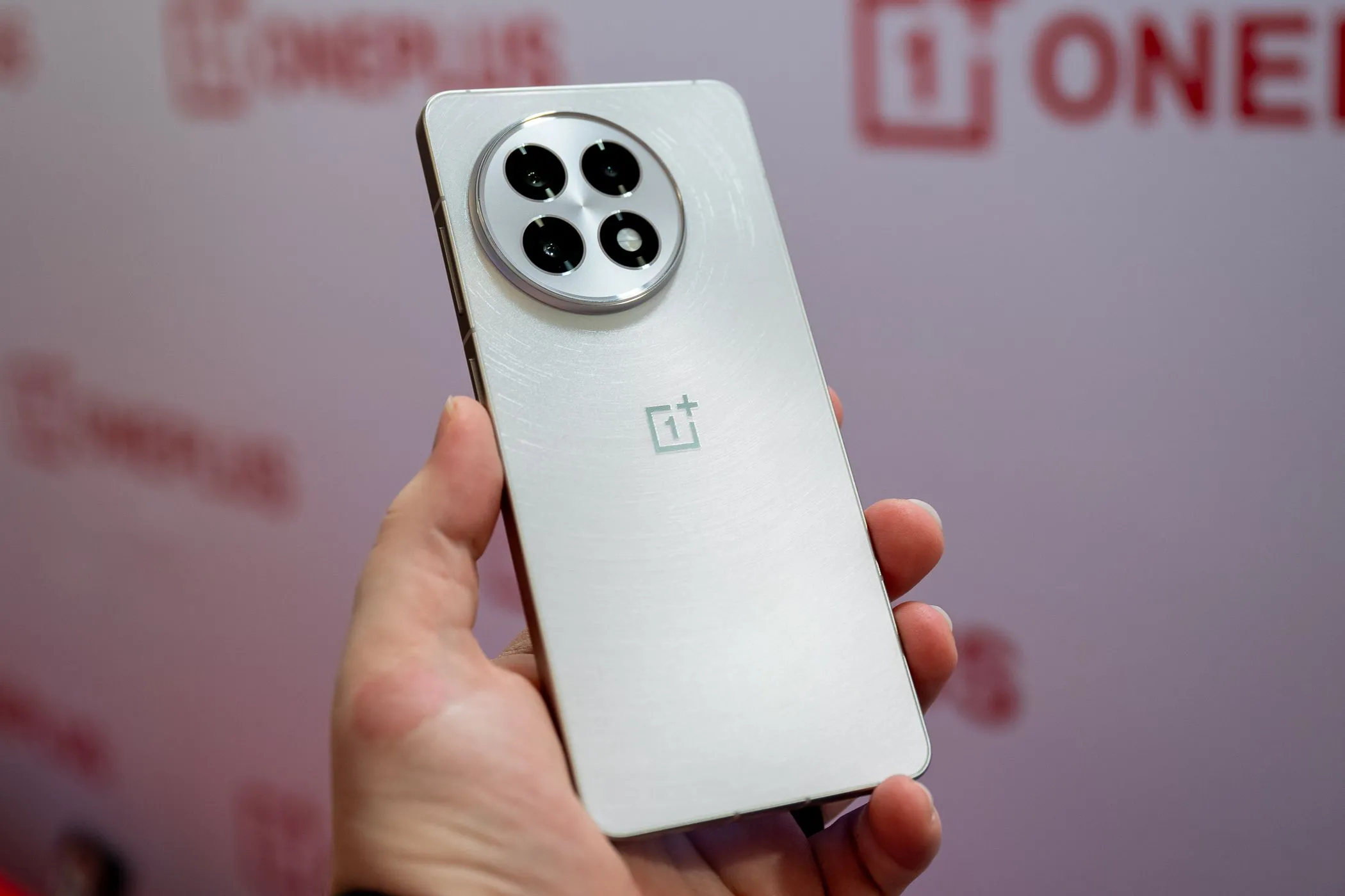 Một người đang cầm chiếc điện thoại OnePlus 13R màu trắng, thể hiện kích thước và thiết kế tổng thể của thiết bị.