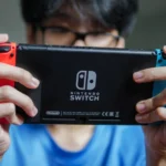 Người đàn ông đang chơi game trên máy Nintendo Switch ở chế độ cầm tay, thể hiện sự tiện lợi khi di chuyển.