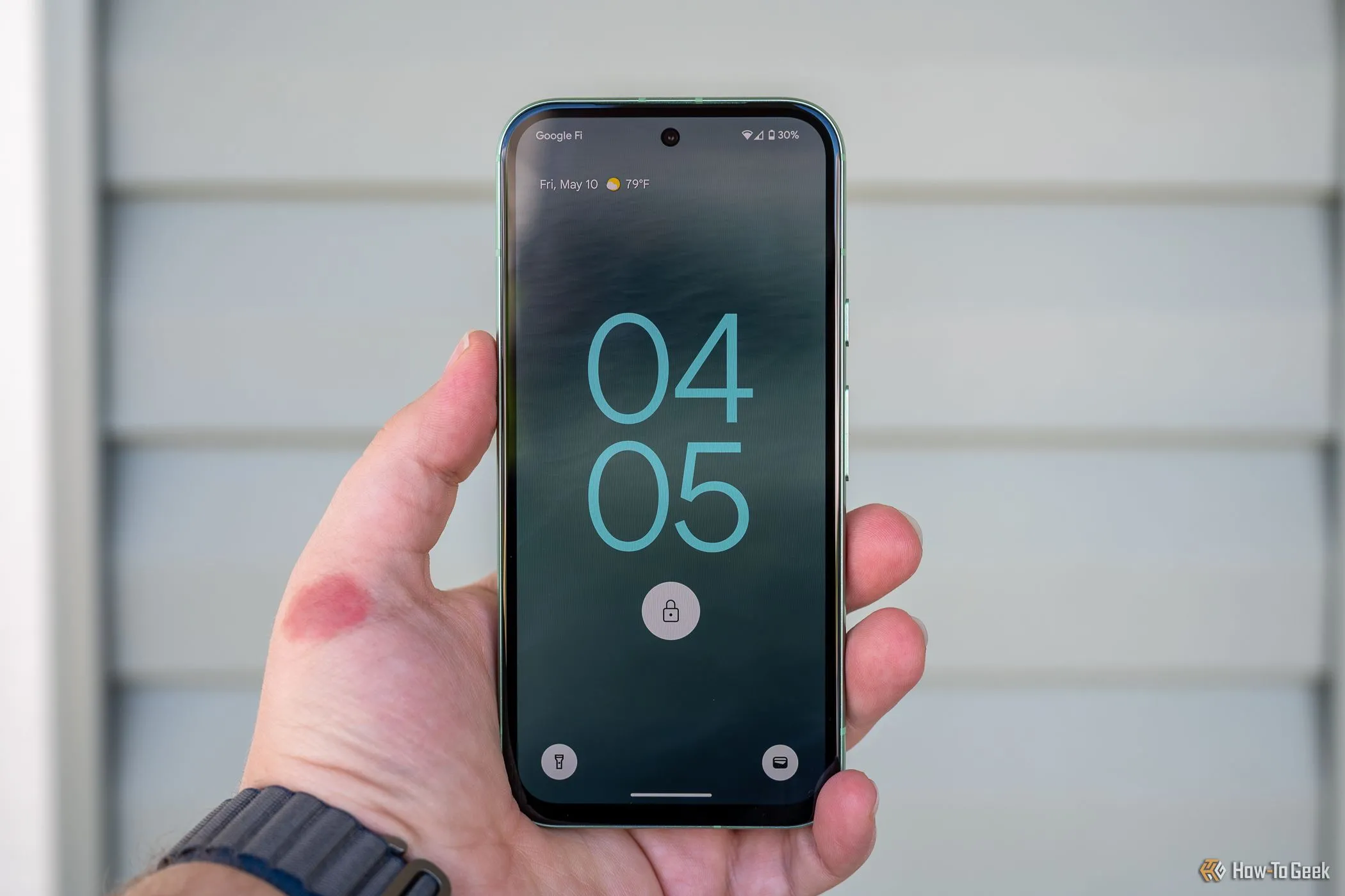 Người dùng cầm điện thoại Google Pixel 8a hiển thị màn hình khóa với giao diện Android 15.