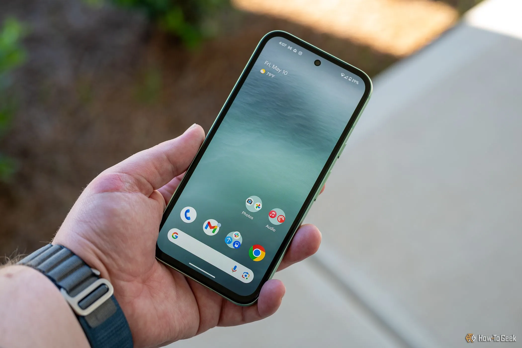 Người dùng đang cầm chiếc Google Pixel 8a màu đen, hiển thị màn hình chính cùng viền màn hình và camera selfie đục lỗ