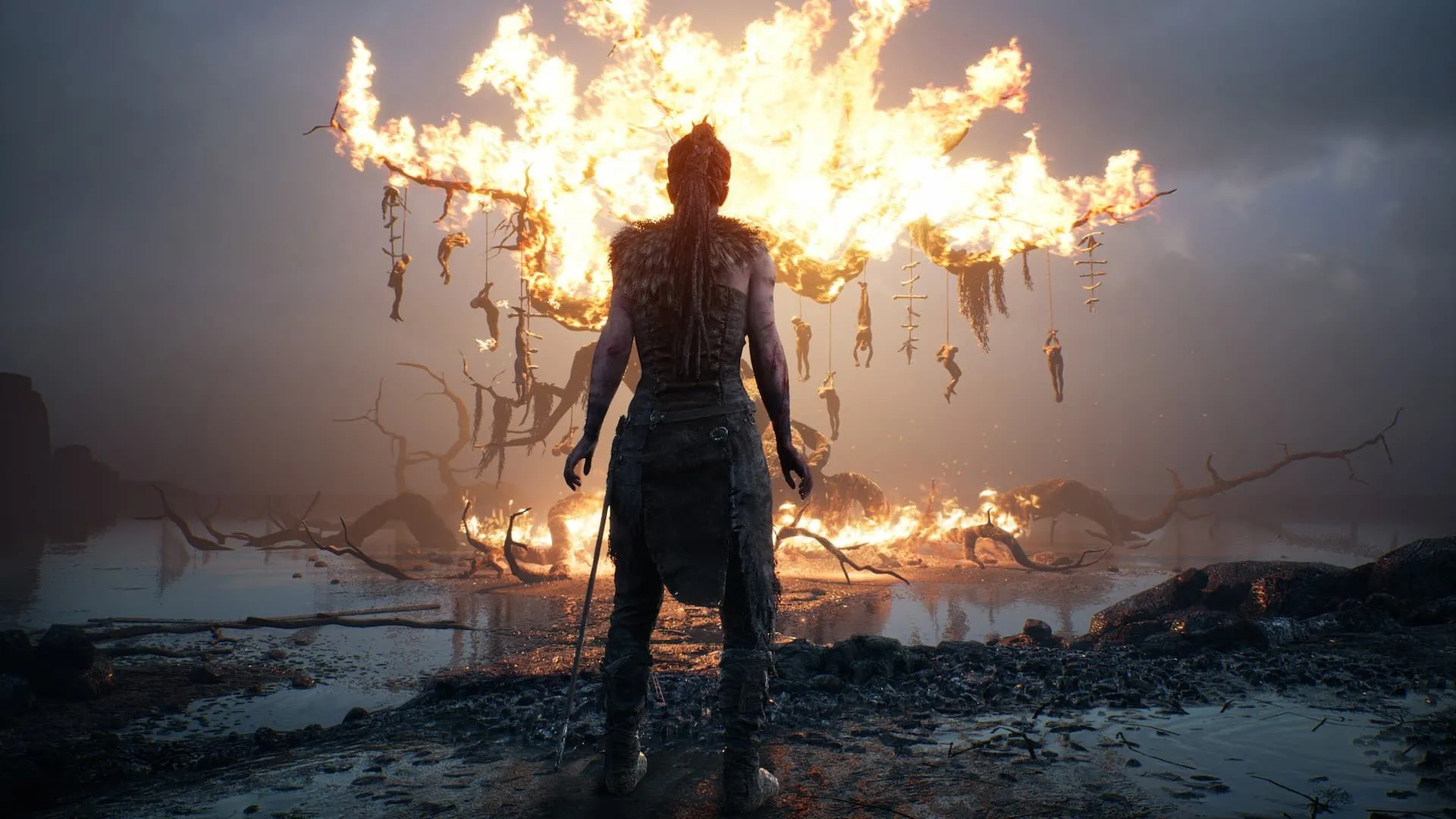 Nhân vật Senua đứng nhìn một cái cây đang cháy rực trong Hellblade Senua’s Sacrifice, thể hiện không khí u ám của game