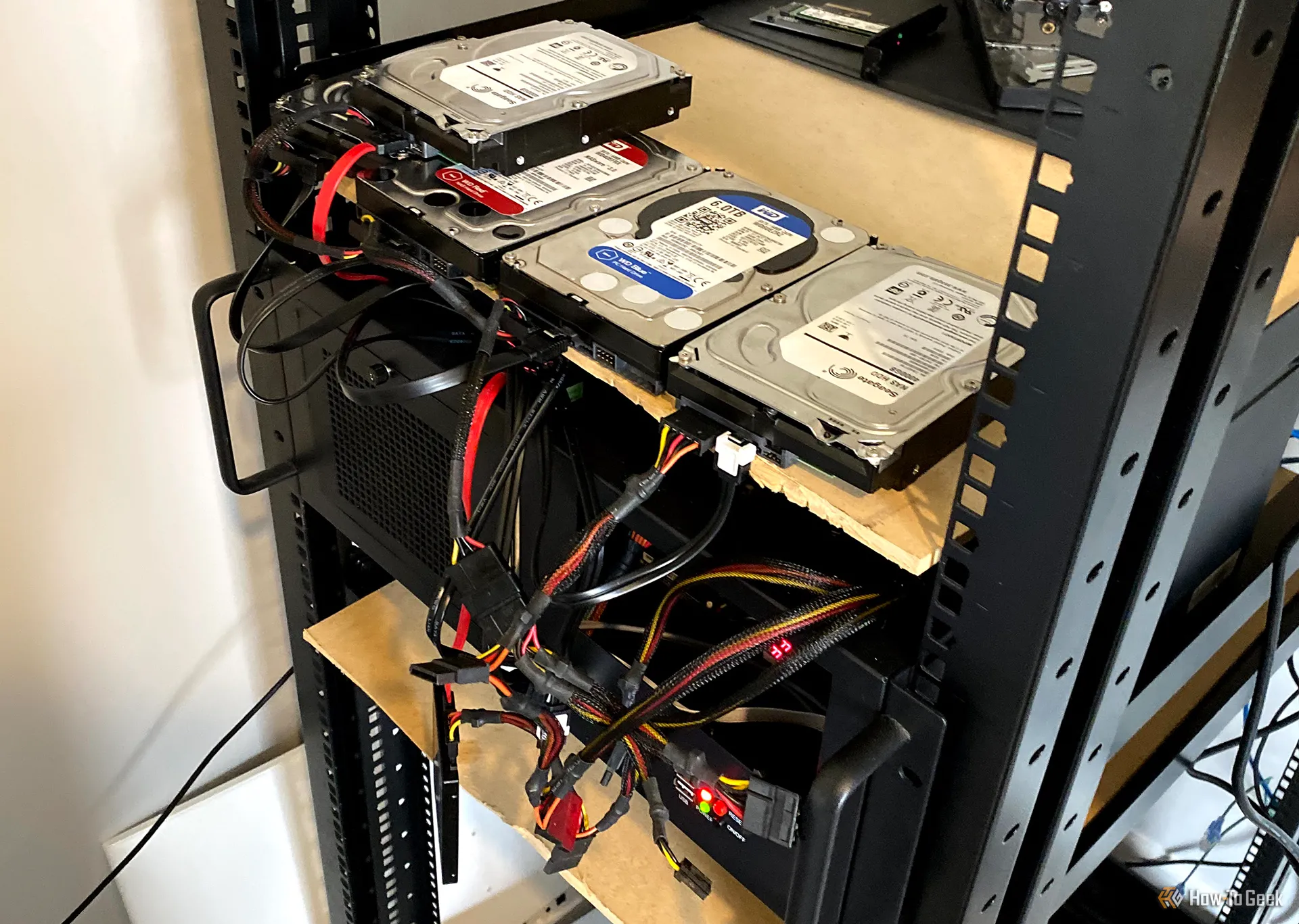 Nhiều ổ cứng đặt trên kệ, kết nối với máy tính để bàn gắn tủ rack, minh họa một hệ thống NAS tự chế từ laptop cũ và ổ cứng ngoài.