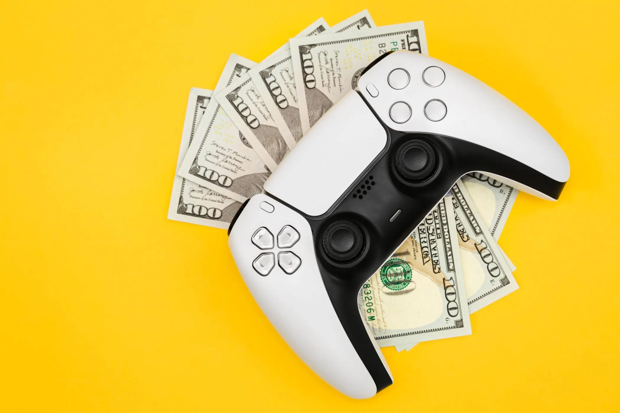 Tay cầm PlayStation 5 đặt trên nhiều tờ tiền 100 đô la, minh họa chi phí phát triển game và giá game tăng cao.