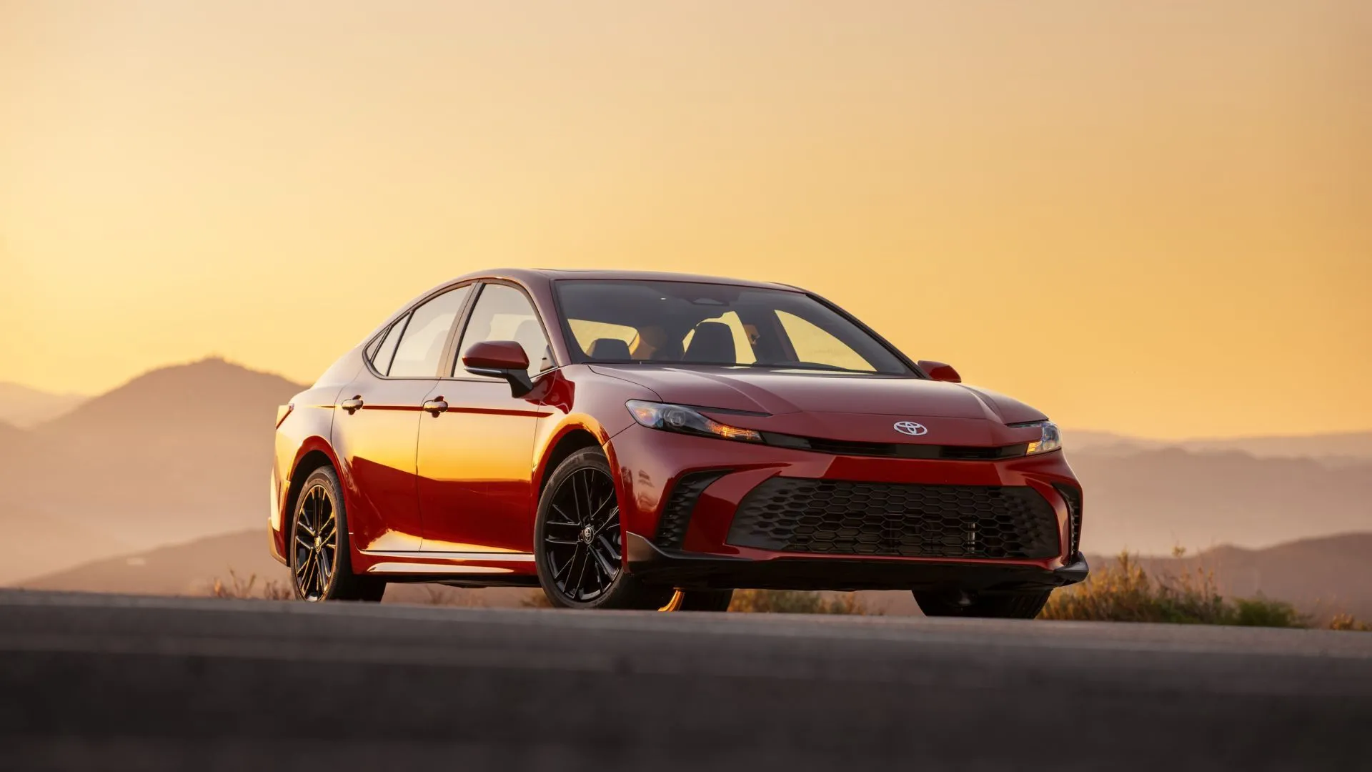 Tổng quan phía trước ba phần tư của một chiếc Toyota Camry 2025 màu đỏ với dãy núi phía sau.